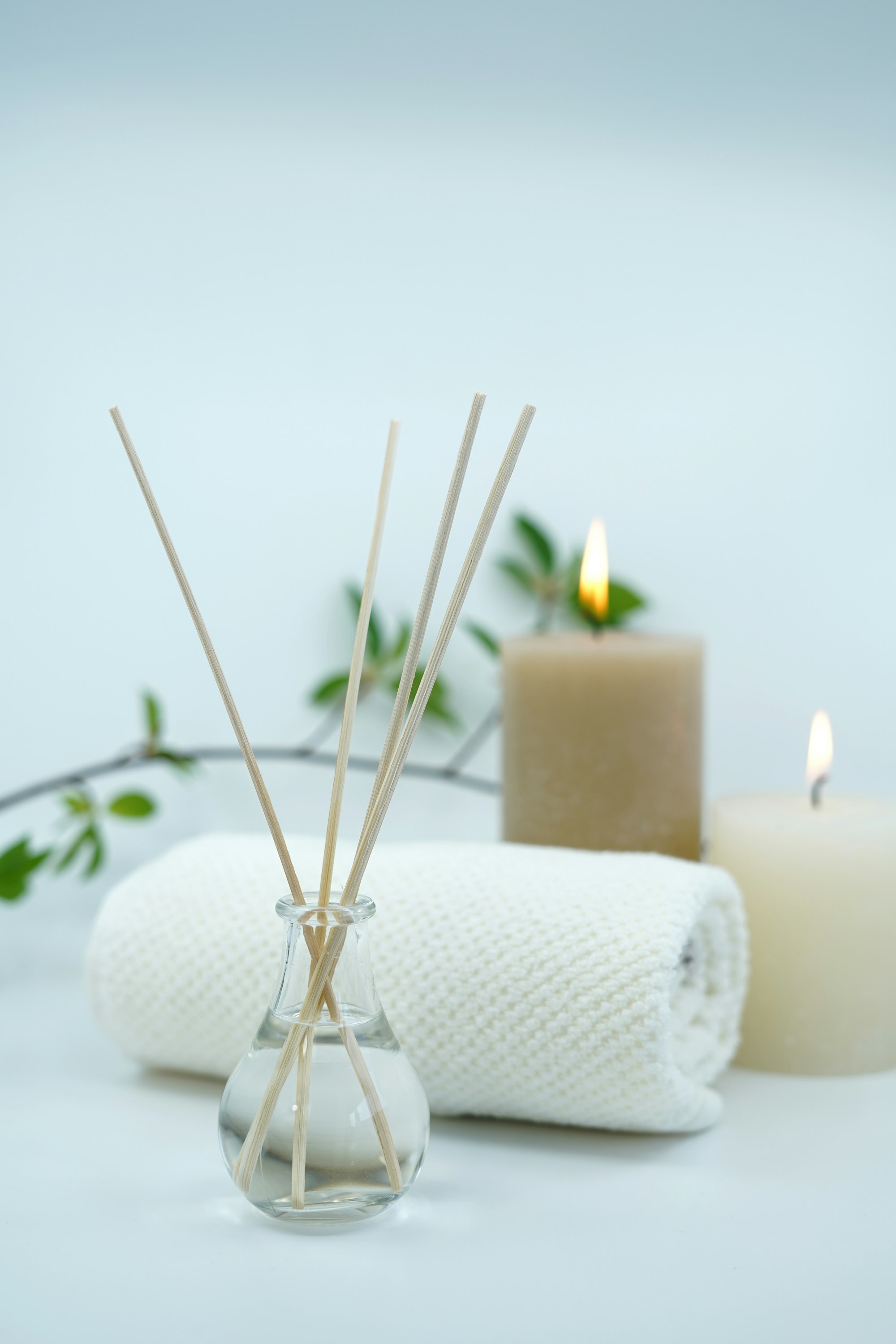 Candles, a reed diffuser and a rolled towel in a calm, softly lit room